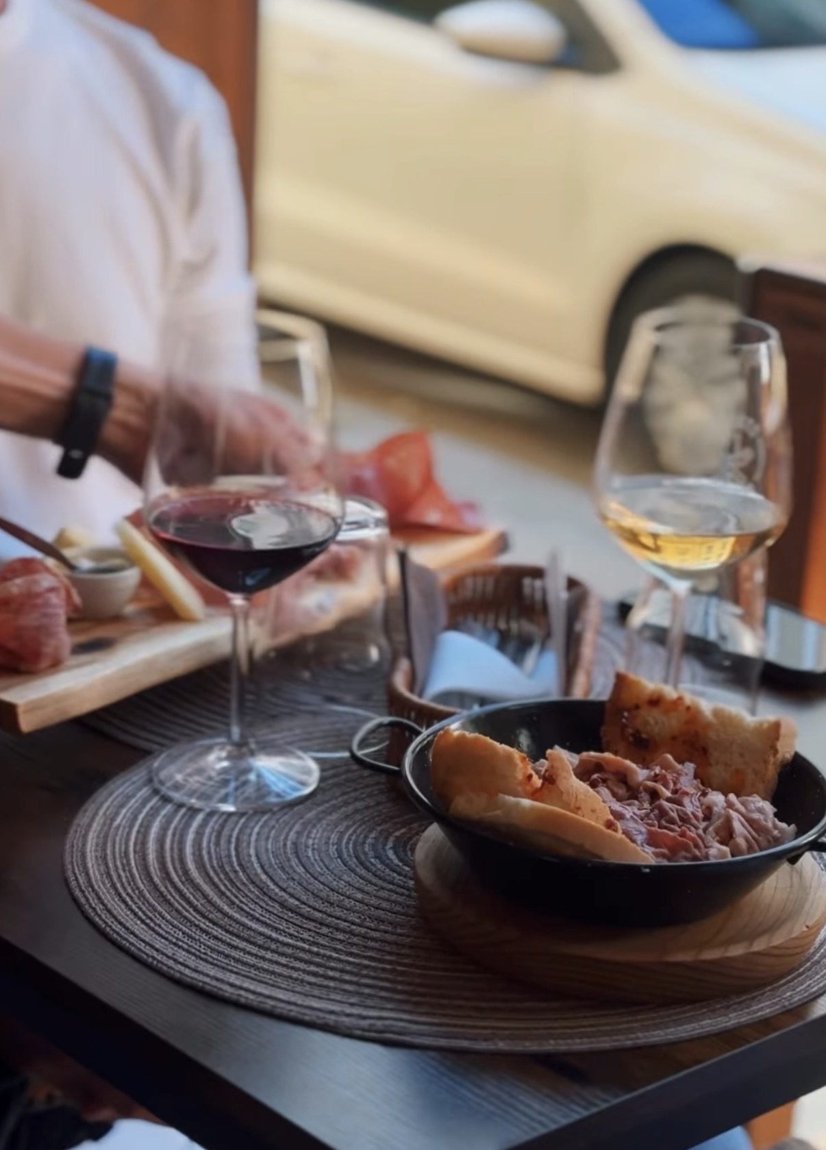 Tavolo all'aperto con carne in padella, due calici di vino e tagliere di salumi e formaggi